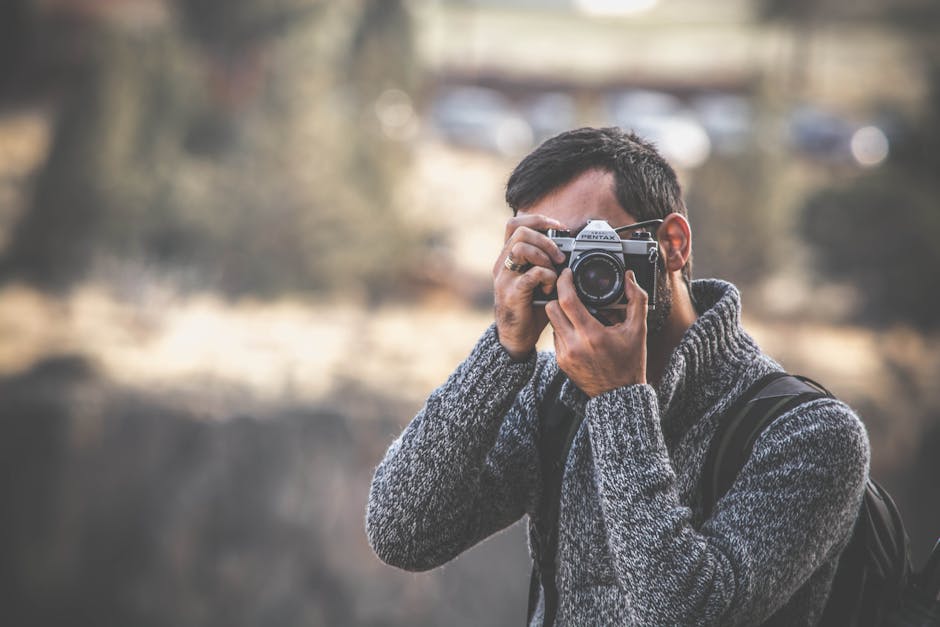 A man with a vintage camera captures outdoor scenes wearing a warm sweater.