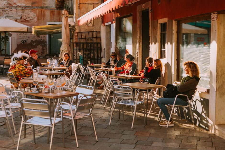 A lively outdoor cafe scene with people enjoying sunny weather in a European alley.