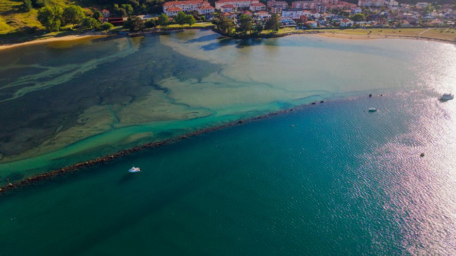 A scenic aerial view of a coastal village with vibrant blue and green waters and moored bo