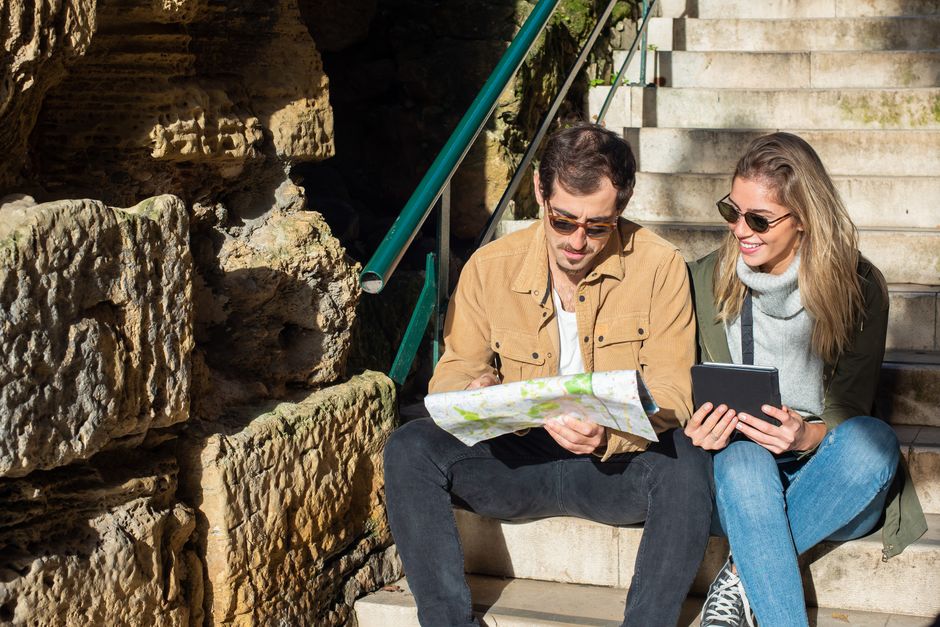 A young couple studies a map and digital tablet on sunny stone steps, planning a travel ro
