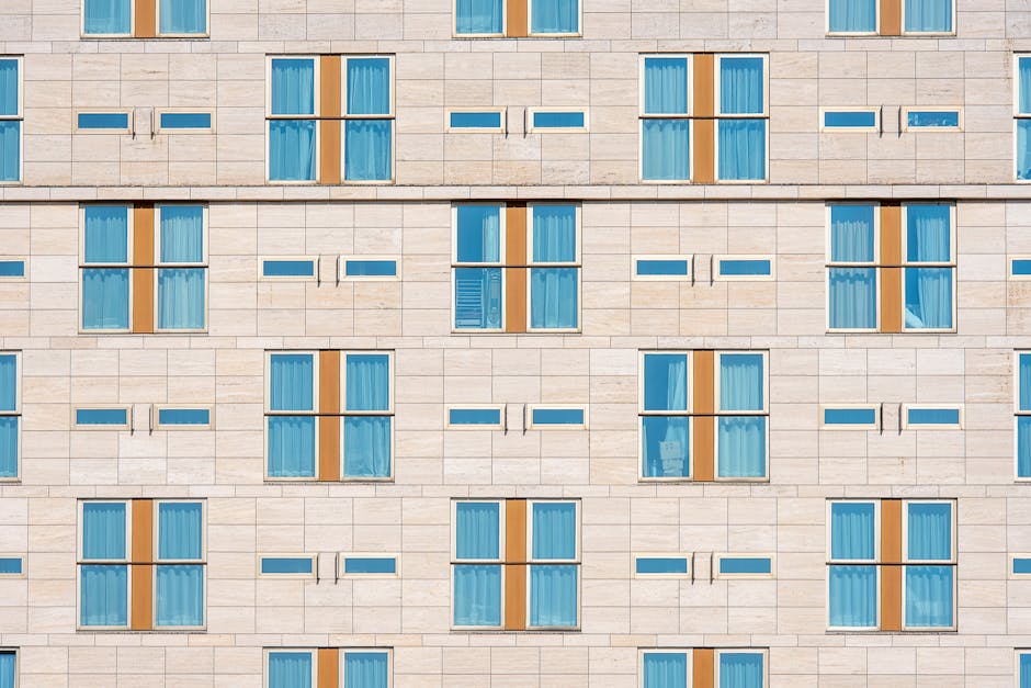 Modern hotel facade showcasing symmetrical design with blue windows and beige stone.