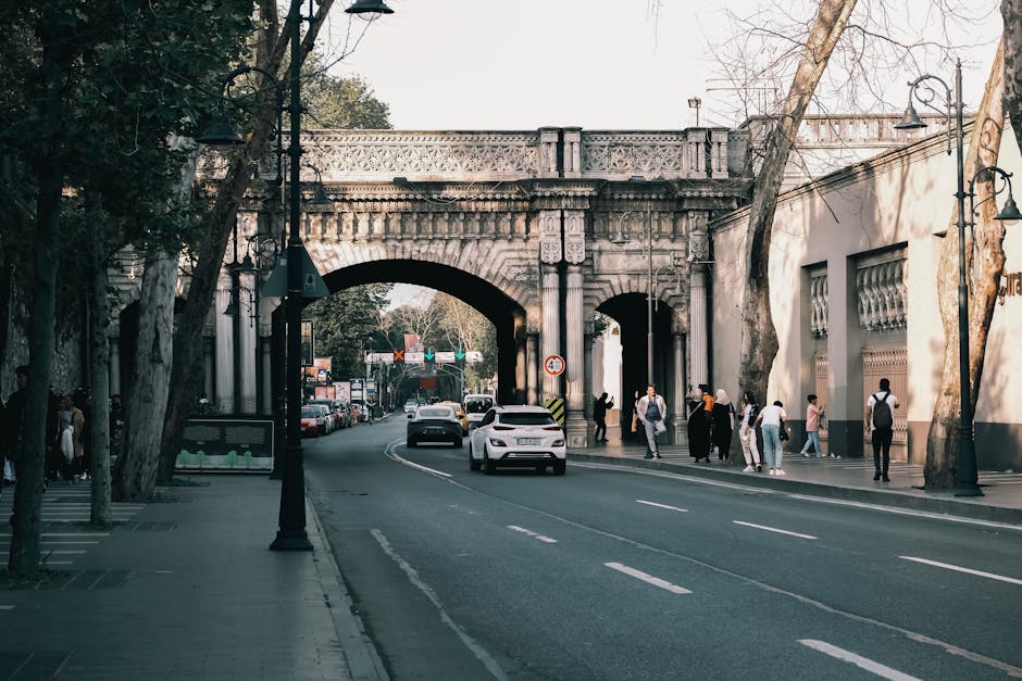 Street scene in Istanbul with cars and pedestrians near a historic archway.
