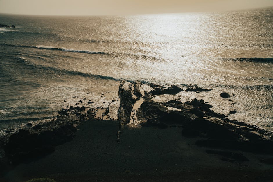 Aerial view of sunlit rocky coastline at Lanzarote, capturing shimmering waters and rugged beauty.