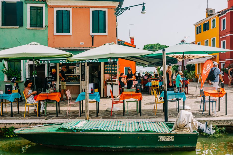 Vibrant umbrellas and tables at a lively outdoor café in picturesque Burano, Italy.